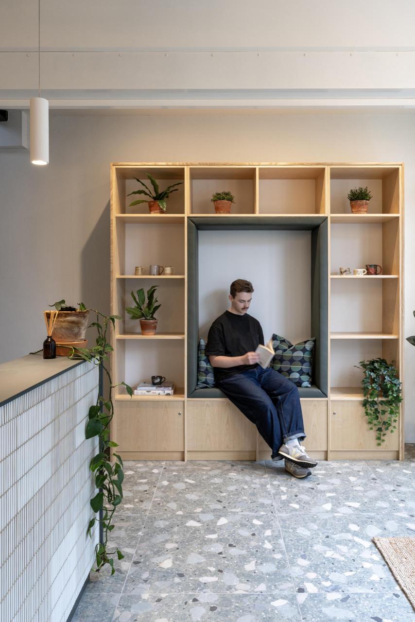 Man sitting in storage and seating nook made from ash and green leather with 4 lockable cupboards